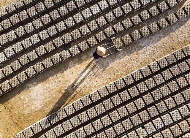 Aerial view of a worker pushing a cart between rows of stacked bricks